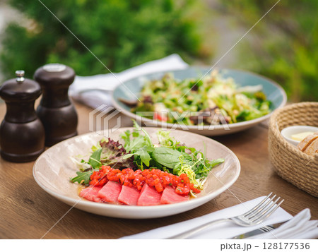 Tuna fillet with strawberry concasse and green salad with fresh herbs and teriyaki sauce in rustic plate. Delicious food in summer sunny day outdoor of restaurant or cafe terrace 128177536