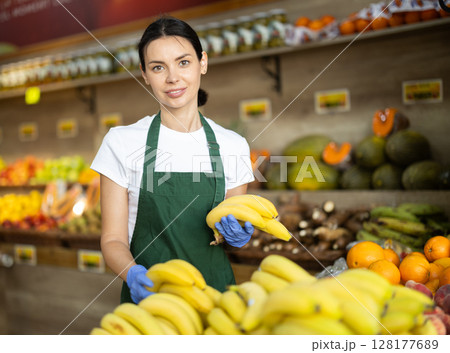 Positive female seller offers to buy ripe tasty bananas in grocery department of supermarket Positive female seller offers to buy ripe tasty bananas in grocery department of supermarket 128177689