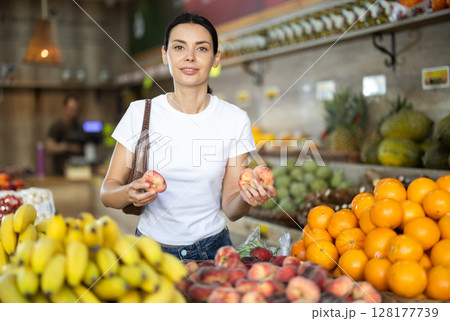 Focused woman shopping in organic food store, choosing flat peaches 128177739