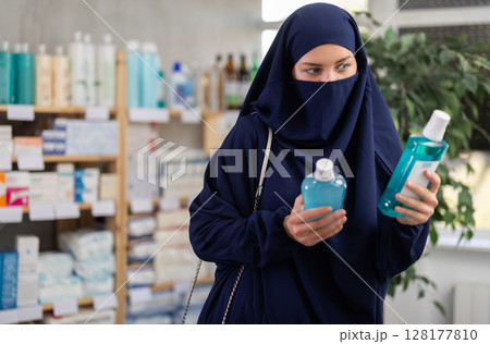 Young Muslim woman client choosing mouthwash in drugstore 128177810