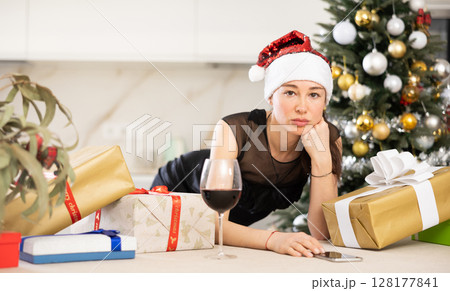 upset young girl in santa hat sits in kitchen. 128177841