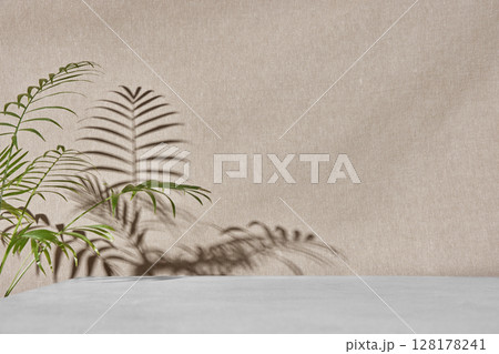Green plant branches on ceramic table with beige fabric background under sunlight. 128178241