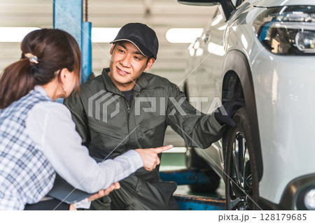 自動車の前で会話する自動車整備士の男性と事務服姿の女性フロント,事務員 自動車の前で会話する自動車整備士の男性と事務服姿の女性フロント,事務員 128179685