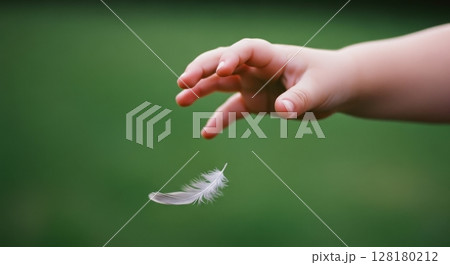 Small child hand reaching out to a soft white feather gently floating down 128180212