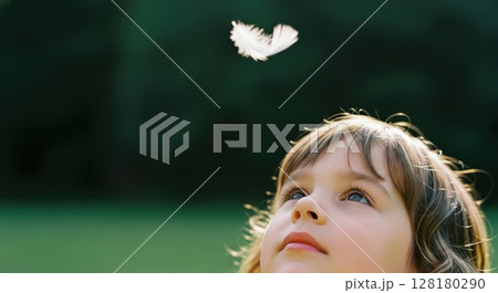 Innocent young girl looking up at a white feather falling with wonder outdoors 128180290