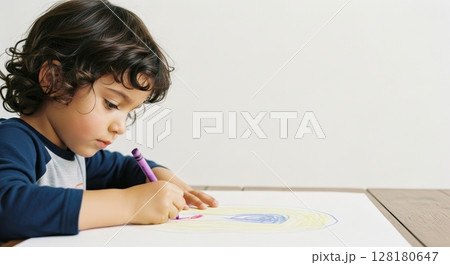 Young boy with curly hair intently drawing with crayon on white paper 128180647