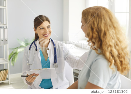Female doctor with happy, friendly smile puts hand on shoulder of young woman to support her Female doctor with happy, friendly smile puts hand on shoulder of young woman to support her 128181502