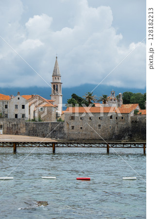 Budva, Montenegro picturesque old town and fortress walls architecture. Stunning showcasing historic stone buildings with red-tiled roofs traditional house. Spire of the chapel of The Church of Sveti Budva, Montenegro picturesque old town and fortress walls architecture. Stunning showcasing historic stone buildings with red-tiled roofs traditional house. Spire of the chapel of The Church of Sveti 128182213
