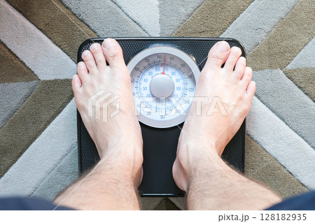 Legs of men standing on scales weight background fitness room. Concept of healthy lifestyle and sport Legs of men standing on scales weight background fitness room. Concept of healthy lifestyle and sport 128182935