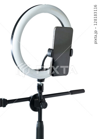 Round LED ring light with a cellphone on a phone holder isolated over a white background. Vlogging or live streaming equipment. Mockup or Copy space 128183116