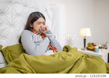 Indonesian southeast asian woman in a blanket sitting on the bed at home and coughing. Suffer from fever, flu, and cold. Healthcare concept 128183296