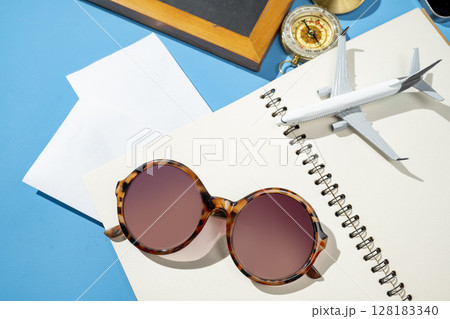 Small chalkboard, airplane, compass, notebook, and sunglasses on a blue background. Mockup or Copy space. Travel adventure, navigation, and planning. Concept for travel, tourism, or vacation Small chalkboard, airplane, compass, notebook, and sunglasses on a blue background. Mockup or Copy space. Travel adventure, navigation, and planning. Concept for travel, tourism, or vacation 128183340
