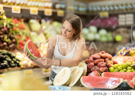 blonde woman standing in a fruit shop and choosing a ripe watermelon 128183562