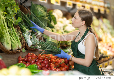 Girl shop seller add bunch of green onion goods on display case in vegetable store 128183566