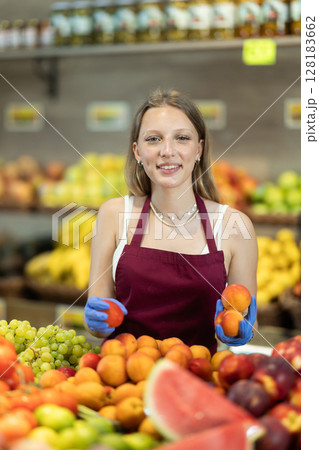 Girl shop seller add peach goods on display case in vegetable store Girl shop seller add peach goods on display case in vegetable store 128183662