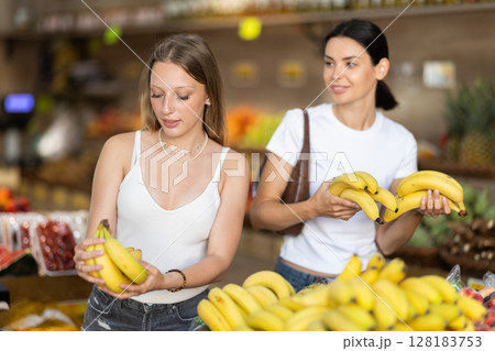 Two women are standing near the counter and choosing bananas 128183753
