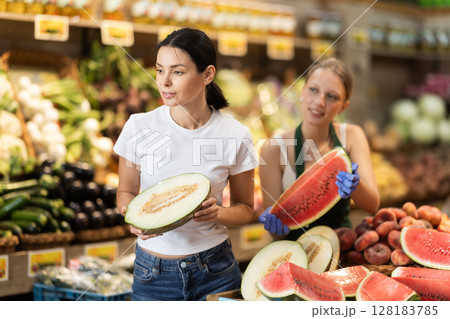 Woman customer in vegetable store examines melon, female seller help 128183785