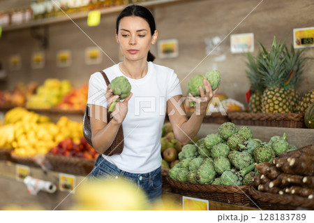 Girl client near vegetable stand in store choose artichoke 128183789
