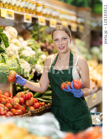 Girl shop seller add tomato goods on display case in vegetable store Girl shop seller add tomato goods on display case in vegetable store 128183811