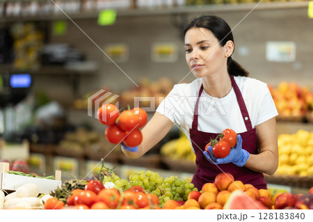 Girl shop seller add tomato goods on display case in vegetable store 128183840