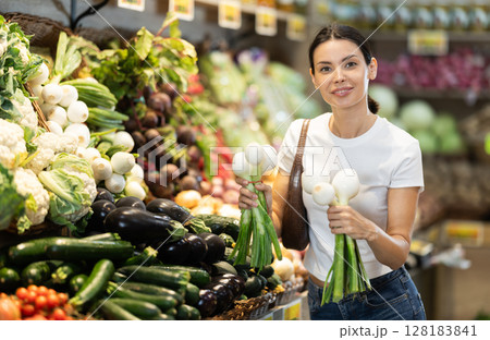 Girl client near vegetable stand in store choose bunch of green onion 128183841