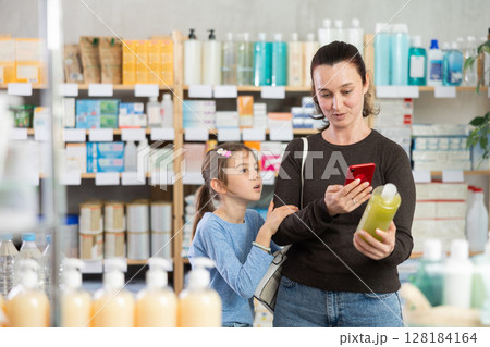 Woman with daughter scanning qr code of shampoo or shower gel Woman with daughter scanning qr code of shampoo or shower gel 128184164