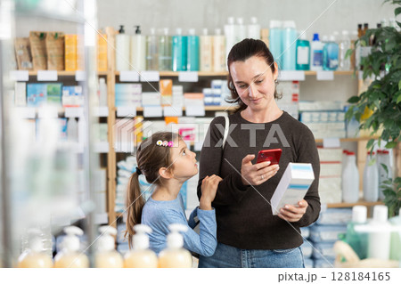 Woman with daughter in pharmacy scans QR code on cream Woman with daughter in pharmacy scans QR code on cream 128184165