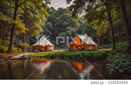 Two tents are set up next to a body of water. The tents are made of canvas and are set up in a forest. The scene is peaceful and serene, with the water reflecting the light of the sun Two tents are set up next to a body of water. The tents are made of canvas and are set up in a forest. The scene is peaceful and serene, with the water reflecting the light of the sun 128185659