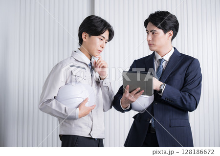 ゼネコンなどの現場で資料を確認する作業服とスーツの男性　打ち合わせで確認する 128186672