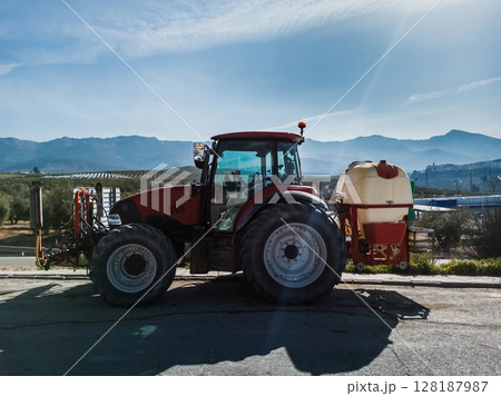 Red Agricultural Tractor with Equipment in Scenic Countryside Red Agricultural Tractor with Equipment in Scenic Countryside 128187987