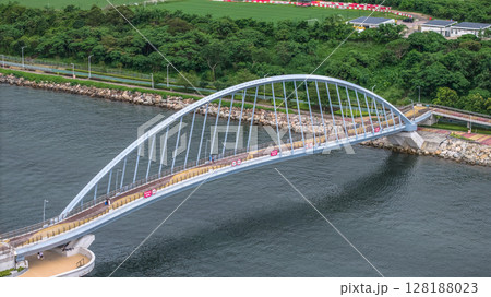 July 1 2025 Elegant Curved Bridge Over Tranquil River in Lush Green Environment 128188023