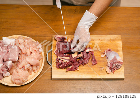 Asian man's hands cutting meat on a wooden cutting board in the kitchen, preparing to cook. Asian man's hands cutting meat on a wooden cutting board in the kitchen, preparing to cook. 128188129
