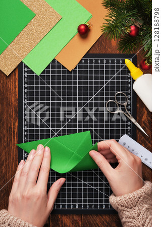 Let's make a simple paper craft. A Christmas tree bookmark. Hands fold the paper. 128188798