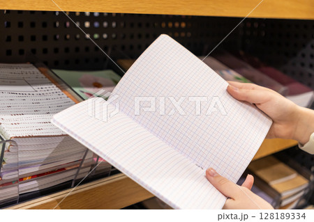 Person's hands carefully holding an open blank grid-lined notebook in a stationery store, ideal for students, office supplies, or creative planning 128189334