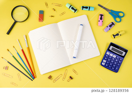 Bright flat lay of colorful school and office supplies, featuring a notebook, pen, and calculator, on a yellow background, promoting learning and creativity 128189356