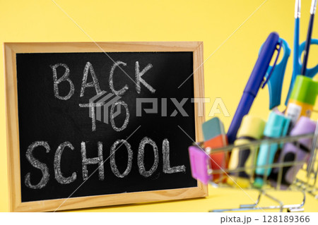 Blackboard displaying 'BACK TO SCHOOL' message alongside a miniature shopping cart filled with vibrant school supplies, symbolizing academic preparation 128189366
