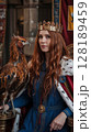 A red-haired queen wearing a crown and royal robe, sitting with a majestic raptor bird in a regal setting. 128189459