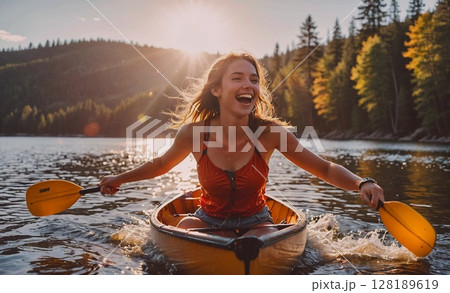 Woman in a red top is paddling a canoe on a lake. She is smiling and enjoying the experience 128189619
