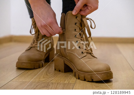 zipping up brown leather boots with laces and chunky heels indoors, close-up of hands adjusting the zipper on the footwear over a wooden floor zipping up brown leather boots with laces and chunky heels indoors, close-up of hands adjusting the zipper on the footwear over a wooden floor 128189945