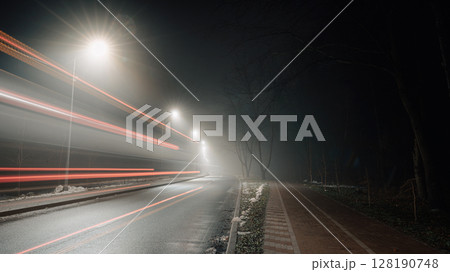 Foggy night road with motion blur of car lights creating dynamic streaks. 128190748