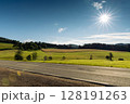 Foothills of the Austrian Alps with asphalt road on foreground and sun on blue morning sky 128191263