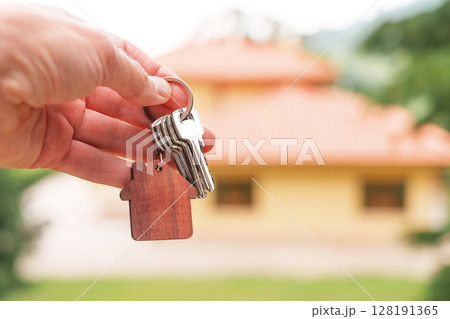 Home keys with wooden house shaped keychain against background of new bungalow in natural ecological area Home keys with wooden house shaped keychain against background of new bungalow in natural ecological area 128191365