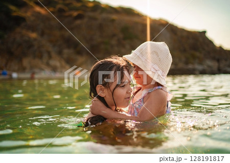 Sisters joyfully embrace while splashing in the warm beach waters 128191817