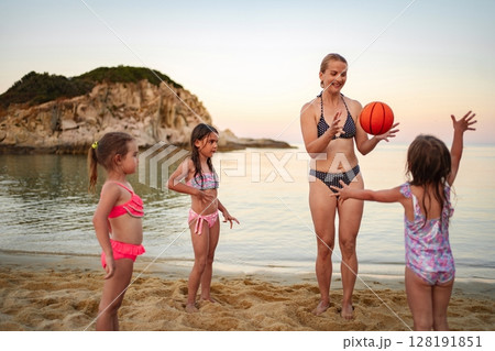Family enjoying a playful sunset moment with a basketball at the beach 128191851