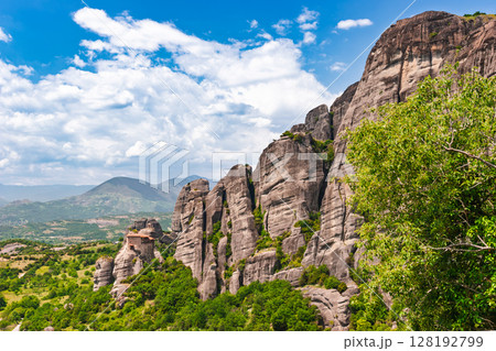 Ancient Meteora monastery perched on cliff edge beside massive rock formation in Greece 128192799