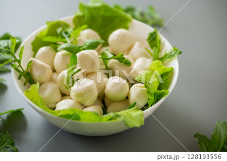 mini mozzarella in white bowl with greens on grey background. Top view 128193556
