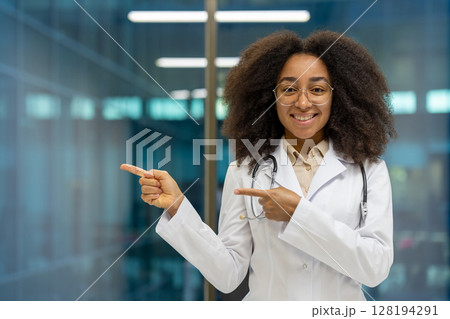 A friendly African-American female doctor in a white coat and stethoscope points to the left side of the frame in a modern hospital 128194291