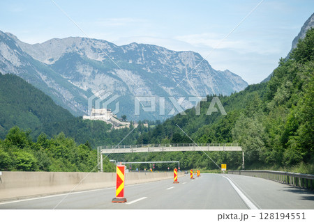 Mountain highway with castle in distance and road construction signs Mountain highway with castle in distance and road construction signs 128194551