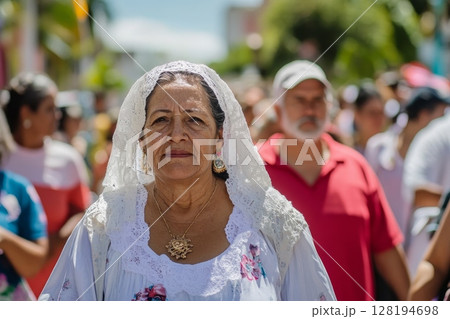 Senior woman wearing white lace headdress and floral dress at outdoor celebration 128194698