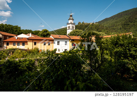 Charming Townscape Of Vipava With Castle View: Colorful Historic Houses And Church Tower Nestled Below Forested Hills With Distant Castle Ruins Under A Clear Blue Sky In Western Slovenia 128195197